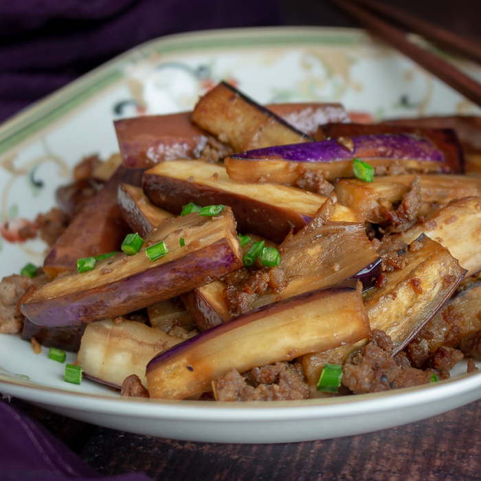 Long eggplant slices stir fried with pork in a Chinese white and green plate. 