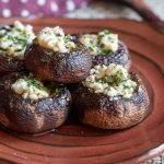 5 delicious feta stuffed portabella mushrooms on a handmade copper colored plate garnished with fresh parsley.