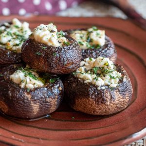 5 delicious feta stuffed portabella mushrooms on a handmade copper colored plate garnished with fresh parsley.