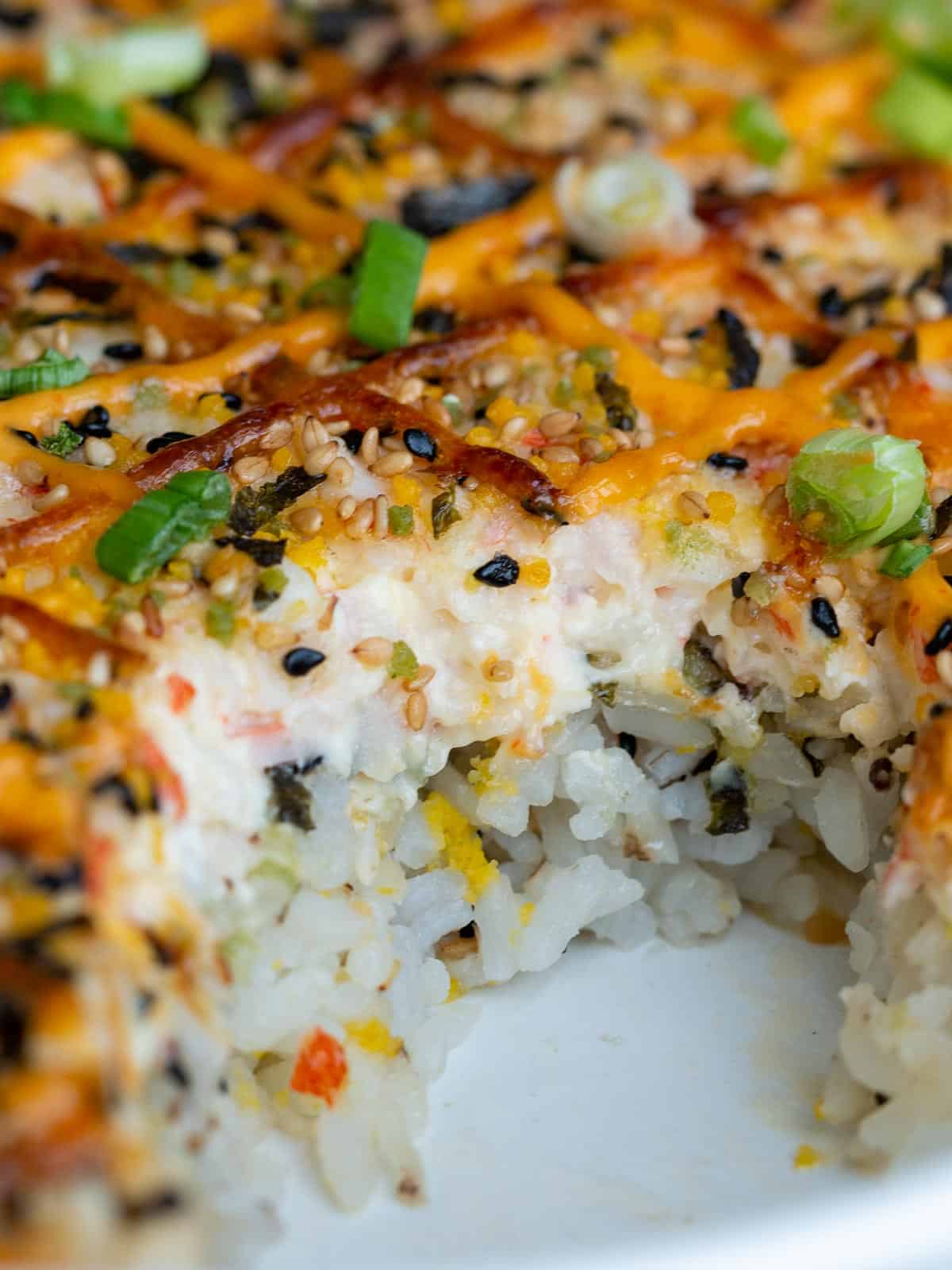 Sushi bake with a scoop out showing the layers of  creamy crab and rice. 