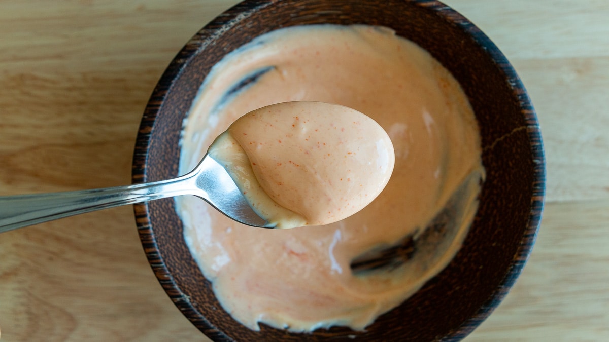 Spicy Mayonnaise in a wooden bowl scooped into a spoon. 