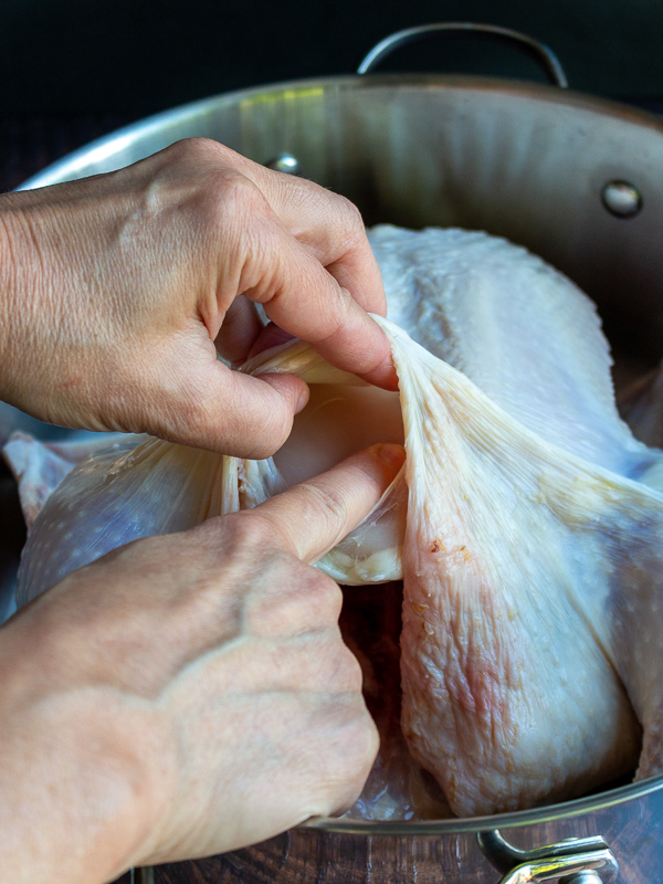 Lifting up the breast skin on the chicken to separate it from the fascia and the chicken breast. 