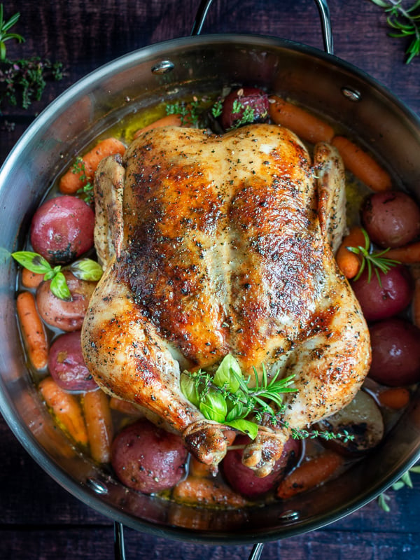 Top Down Shot. Perfectly roasted whole chicken with crispy skin, fresh herbs surrounded by cooked potatoes and carrots. 