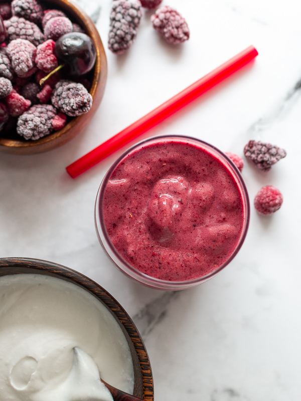 Top down shot of smoothie with on the side frozen berries and coconut whipped cream.