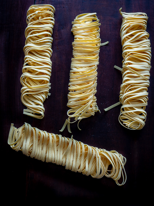 Four dried bundles of dried fettuccine pasta on a dark cutting board. 