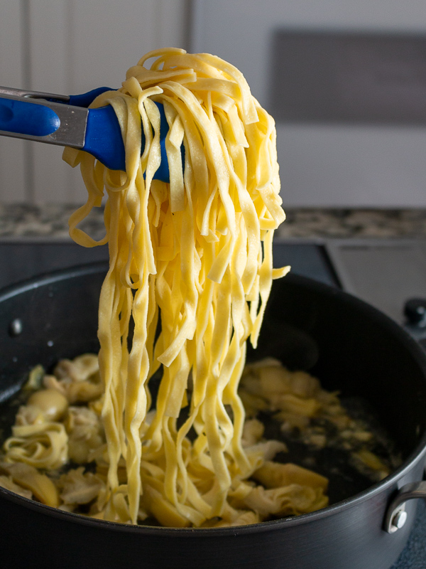 Freshly cooked fettuccine pasta getting transported into the artichoke sauce