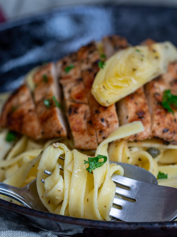 Twirling of fresh aldente fettuccine around a fork with the grilled chicken and artichokes.