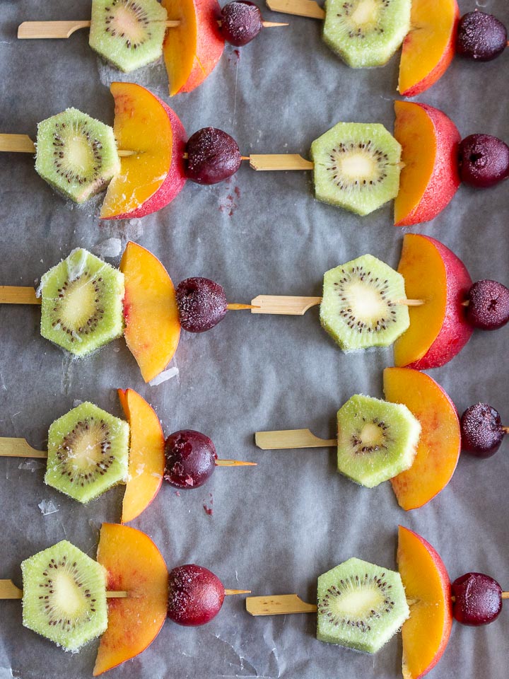 Skewers of kiwi, nectarines and cherries on a baking sheet that have been frozen.