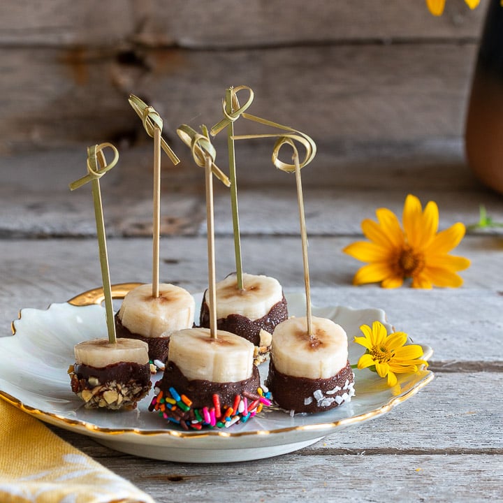 Frozen chocolate covered bananas with sprinkles on a white plate.