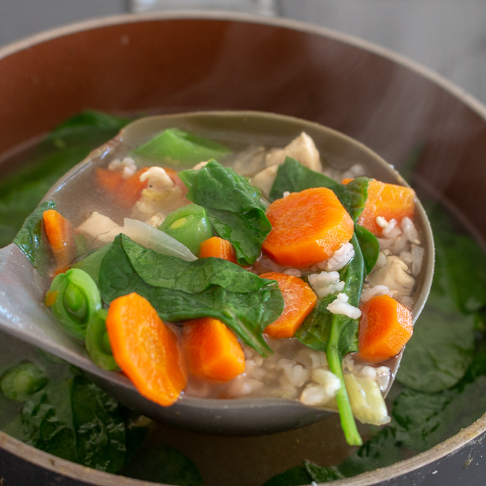 Big scoop of chicken soup with a soup ladle. 