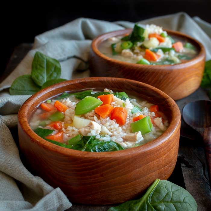 2 bowls of chicken and rice soup in wooden bowls. 