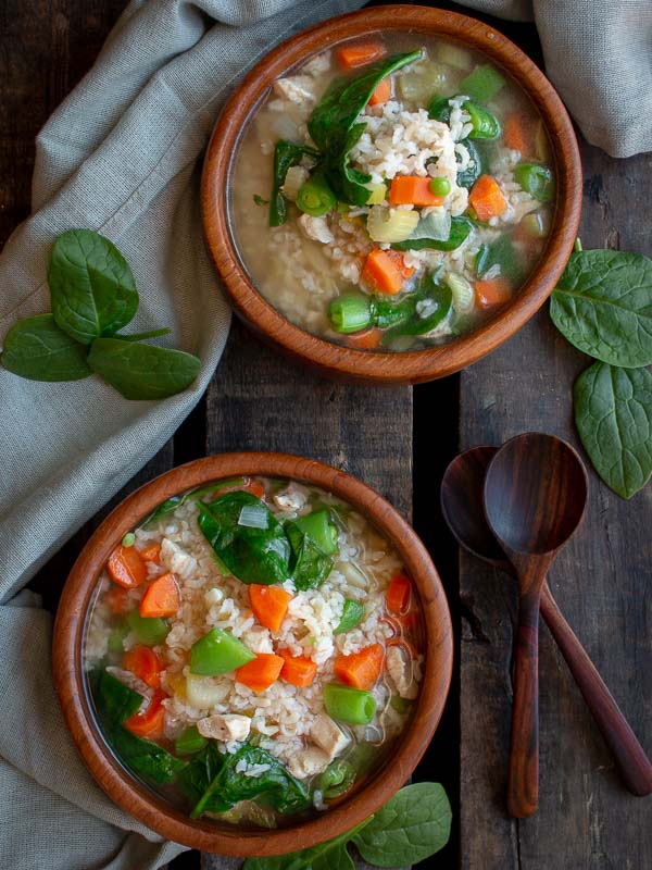 2 bowls of chicken and rice soup in wooden bowls with 2 wooden spoons and a light green napkin.
