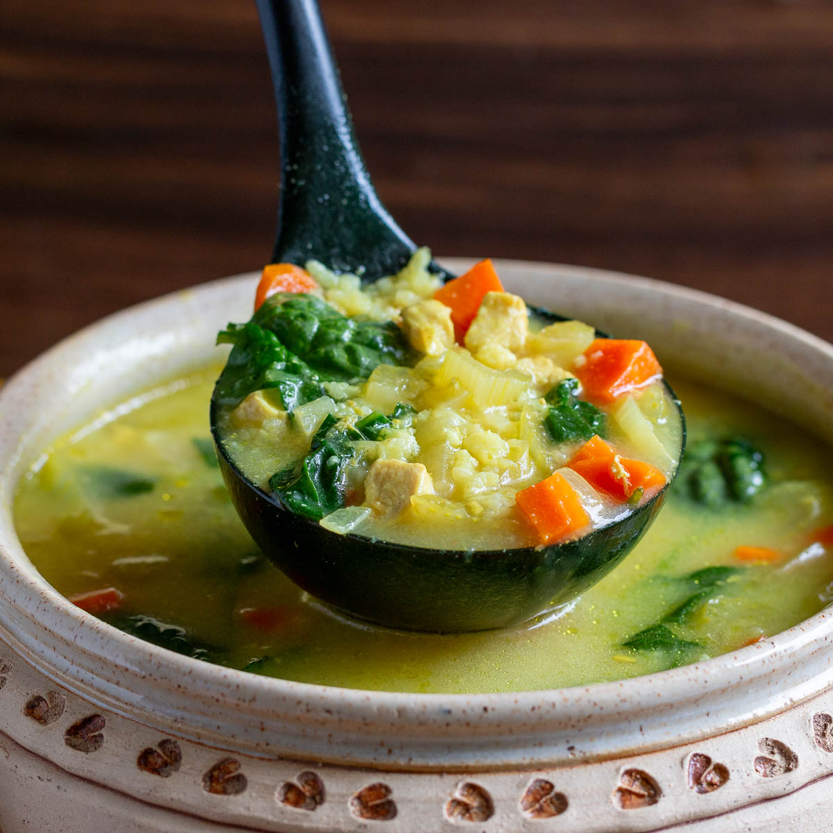 Bite shot of Chicken and rice soup with loads of veggies in a wooden bowl. 