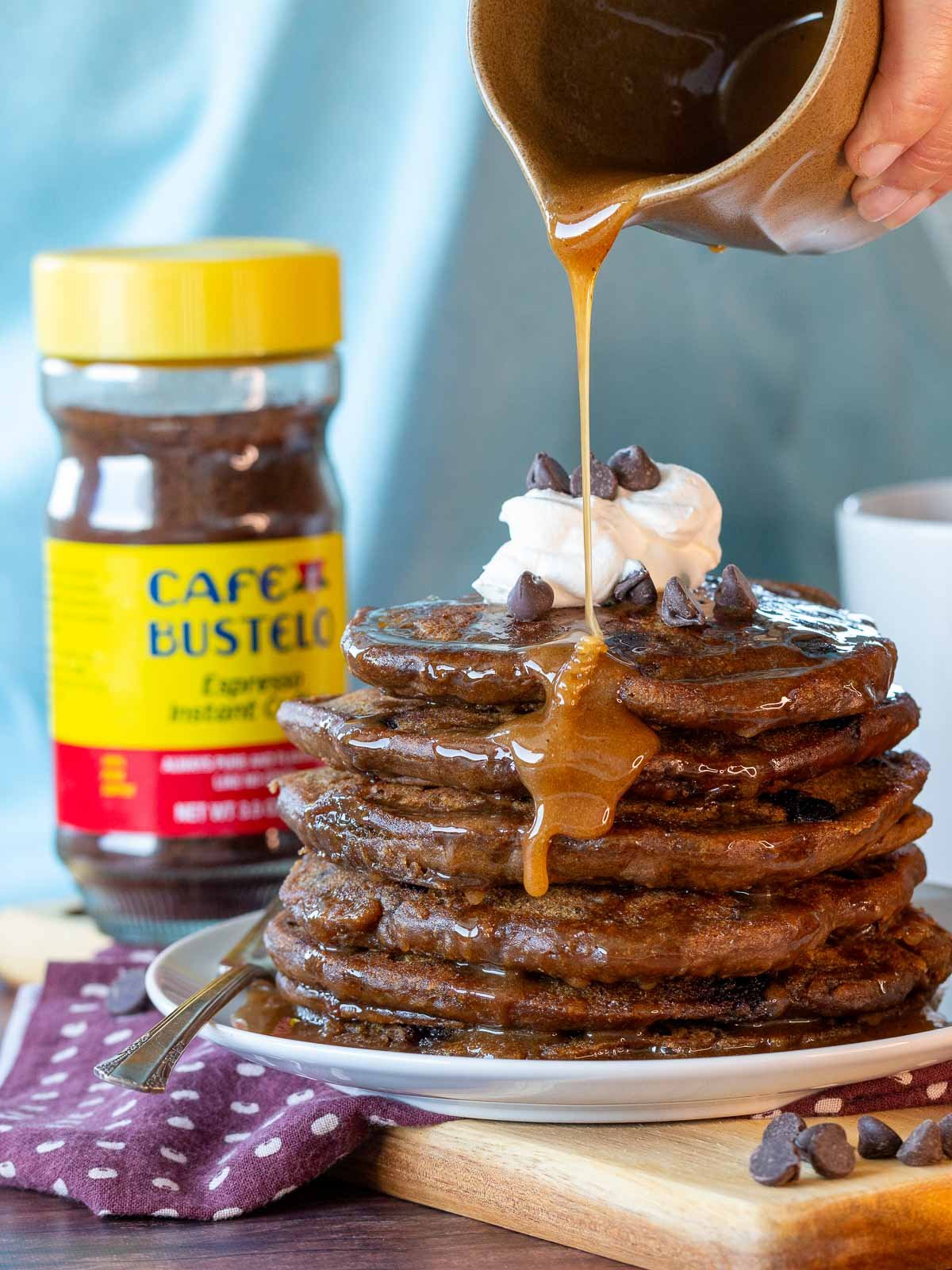 Maple coffee syrup getting poured over a stack of pancakes with coffee and chocolate chips.