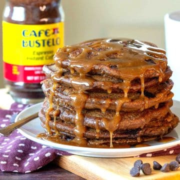 Gluten free coffee pancakes drizzled with maple coffee syrup on a white plate with a cup of coffee.