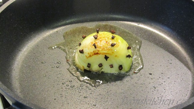 ½ onion studded with whole cloves frying in a pan.