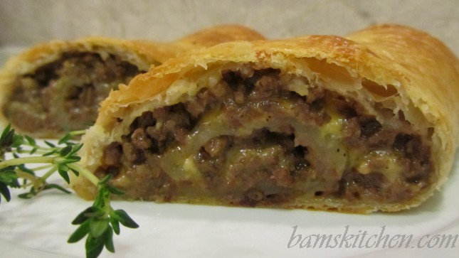 Cheesy puff pastry with meat sliced into on a white cutting board. 