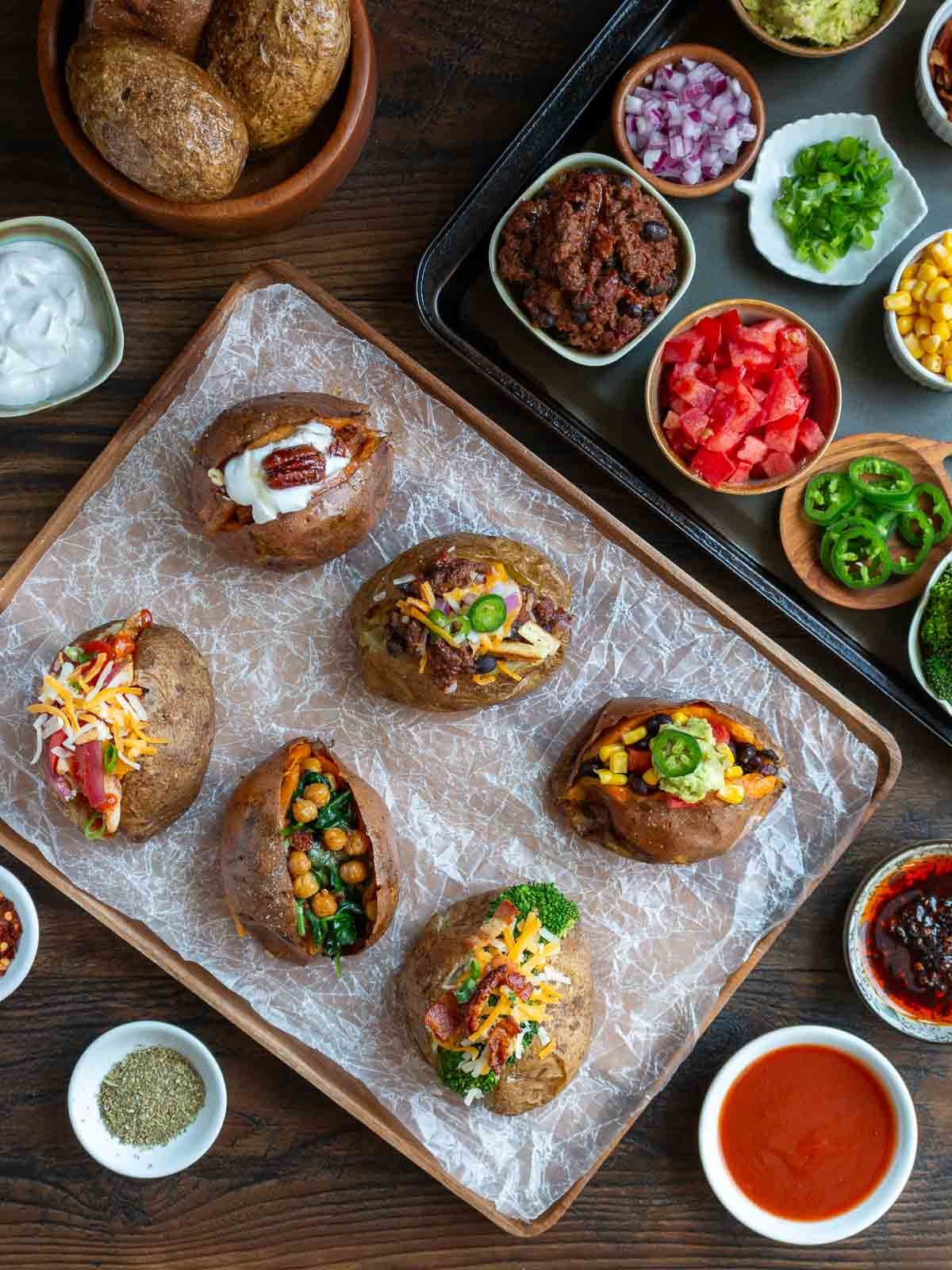 Baked potato bar buffet table set up with baked potatoes, the toppings and 6 example loaded potatoes. 