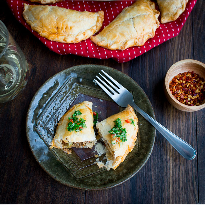 beef filling showing in the cut empanadas with chimichurri on top.