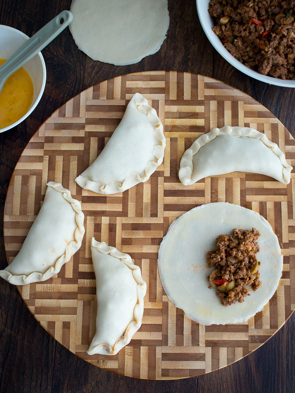 Empanadas getting filled with the beef filling on a cutting board. 