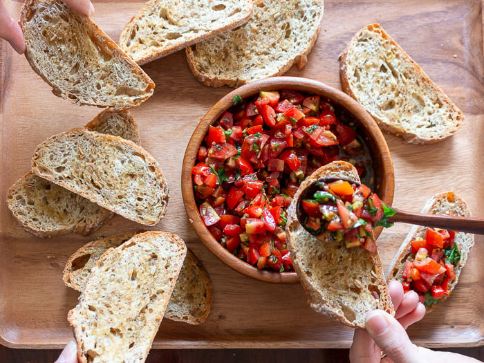 Top down shot showing many friends digging into the shared platter of bruschetta bread.