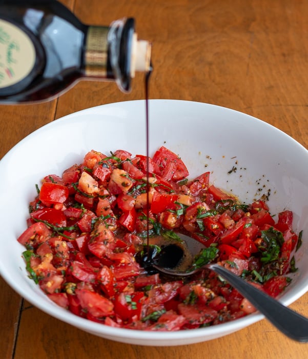 Thick aged balsamic vinegar getting drizzled onto the chopped tomatoes.