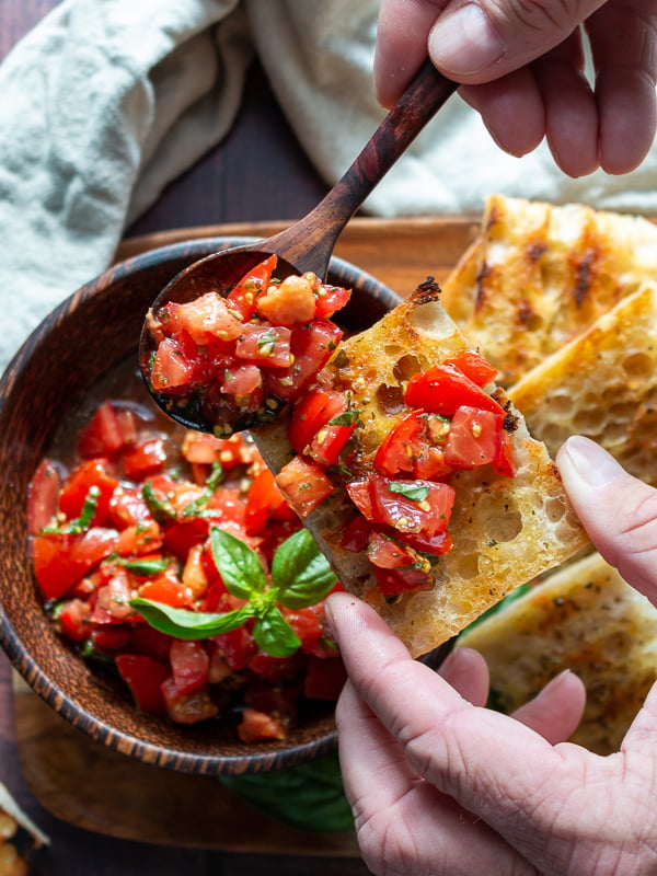 Delicious marinated tomatoes with fresh basil, EVOO and aged balsamic getting scooped on a toasted crostini.