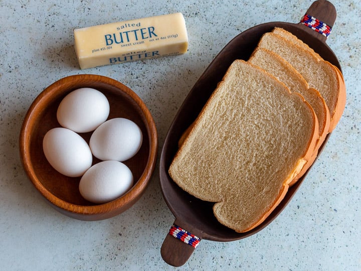 Top down photo of eggs, butter and bread in wooden bowls.