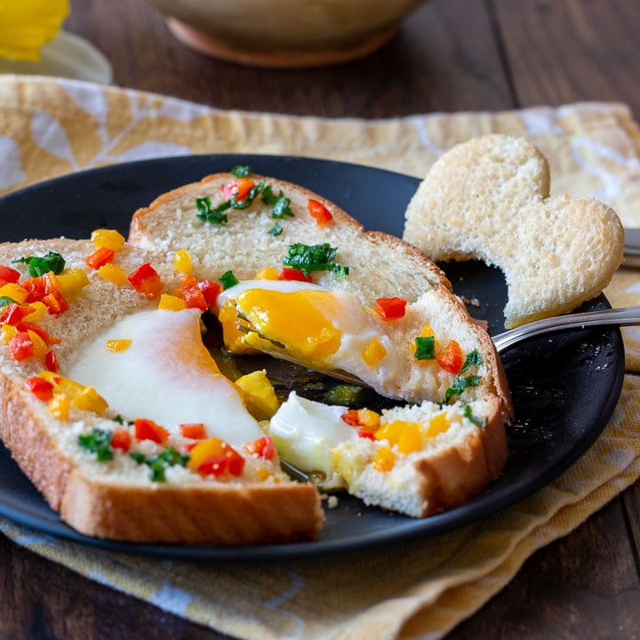 A baked egg in a hole with peppers and parmesan with a drippy egg center.