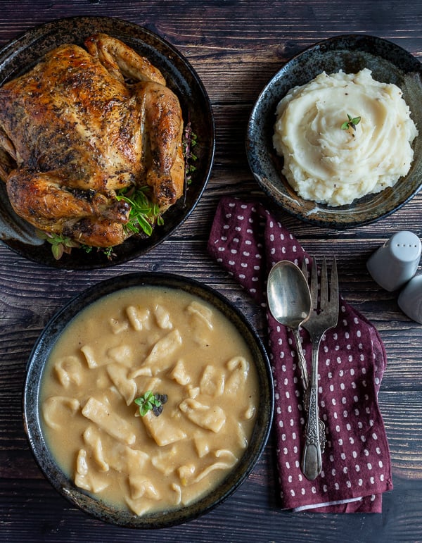 Top down photo of a whole roasted chicken, mashed potatoes and Grandma's sliders in a rich gravy. 