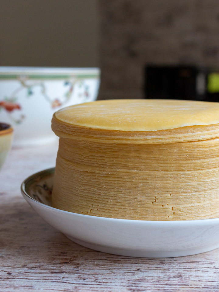 Large stack of Jiaozi wrapper on a white plate.