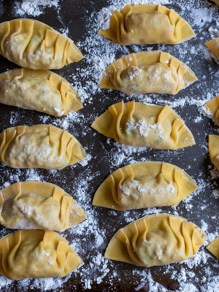 Many prepared dumplings on a baking sheet ready to be cooked. 