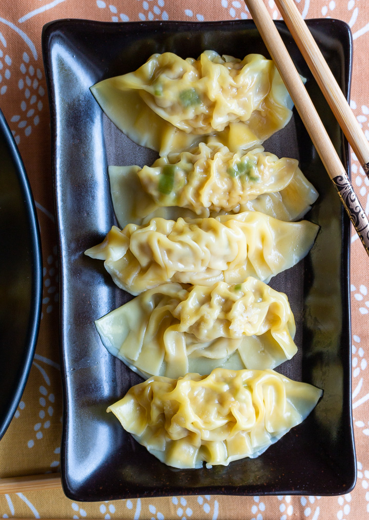 Boiled Chinese dumplings on a black plate.