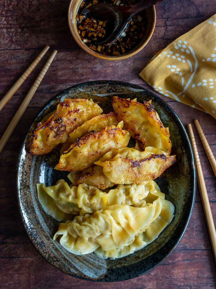 Boiled and pan fried dumplings on a black plate with dipping sauce.