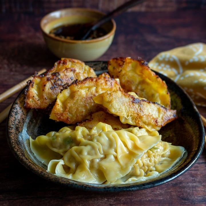 Big both of mixed pan fried dumplings and boiled dumplings with dipping sauce in background.