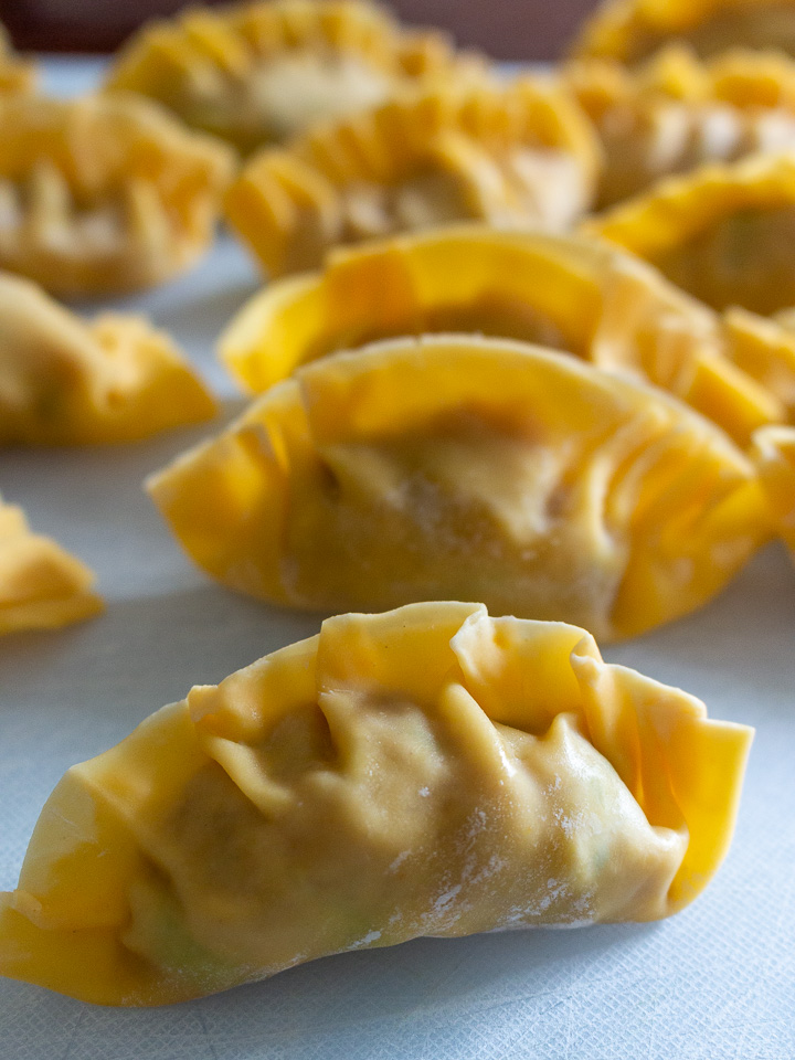 Many Chinese dumplings on a white cutting board ready to be pan-fried.