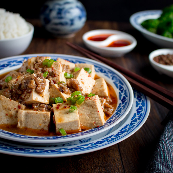 Bowl of mapo tofu in a blue place from Fosan China and chili oil in the background.