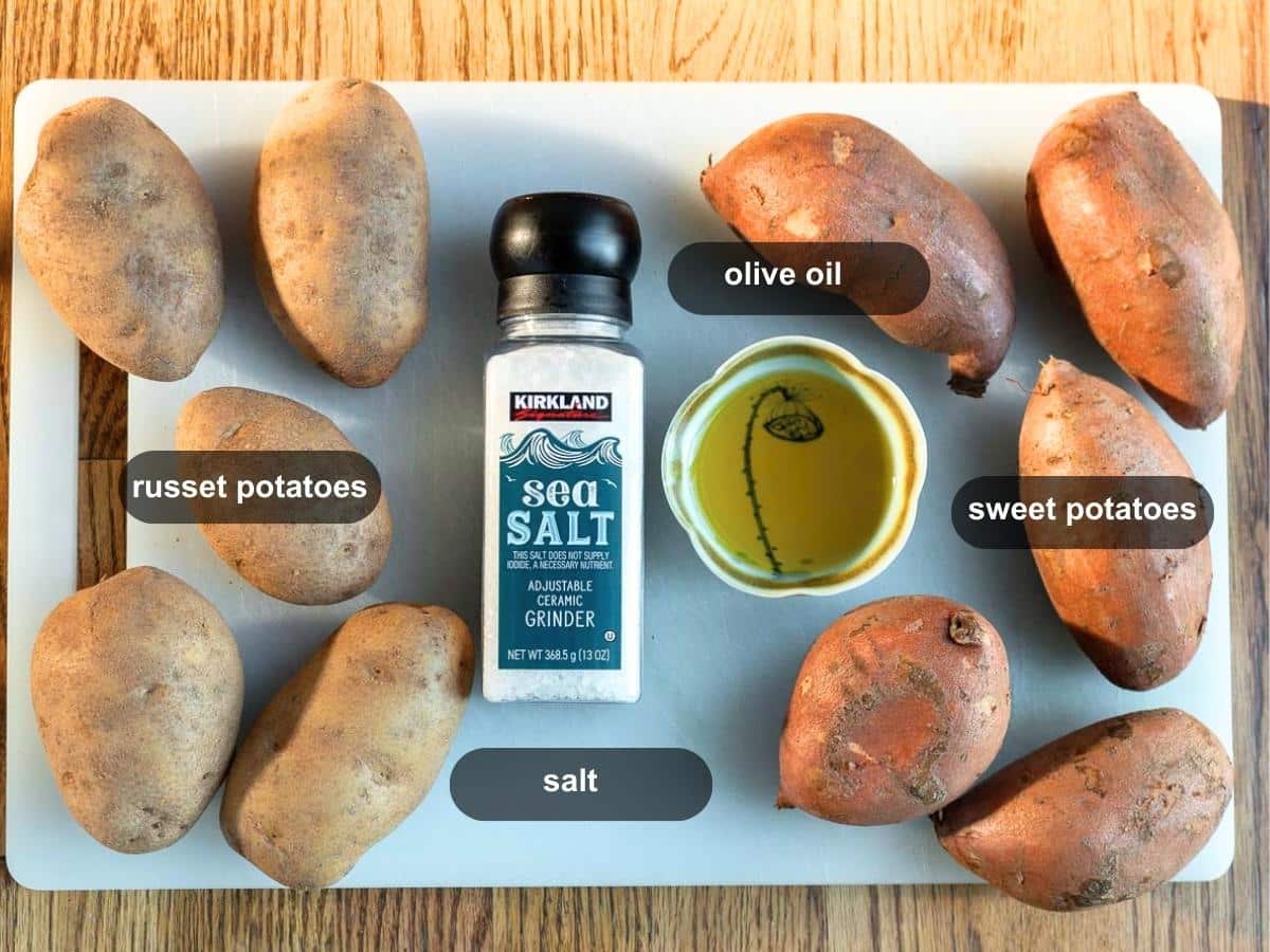 Russet and sweet potatoes, olive oil and salt on a cutting board. 