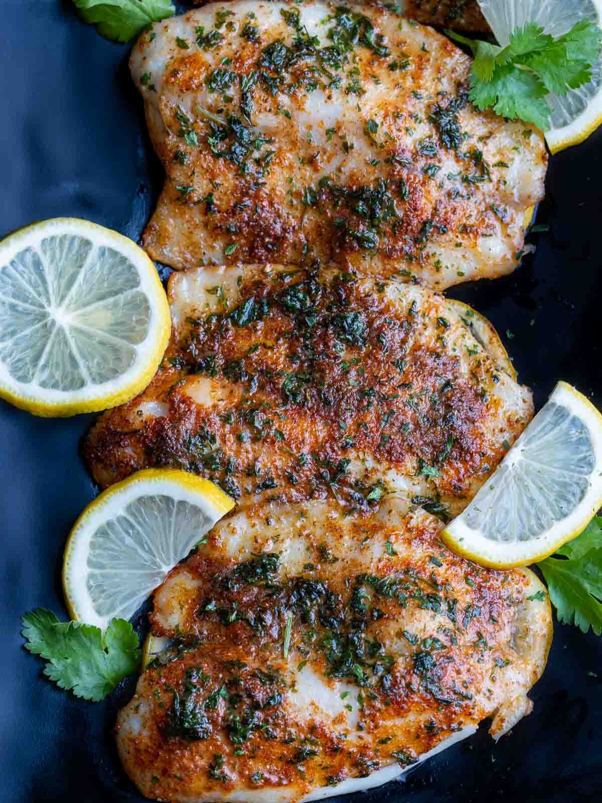 Air fried tilapia fillets on a black plate drizzled with lemon garlic butter sauce.