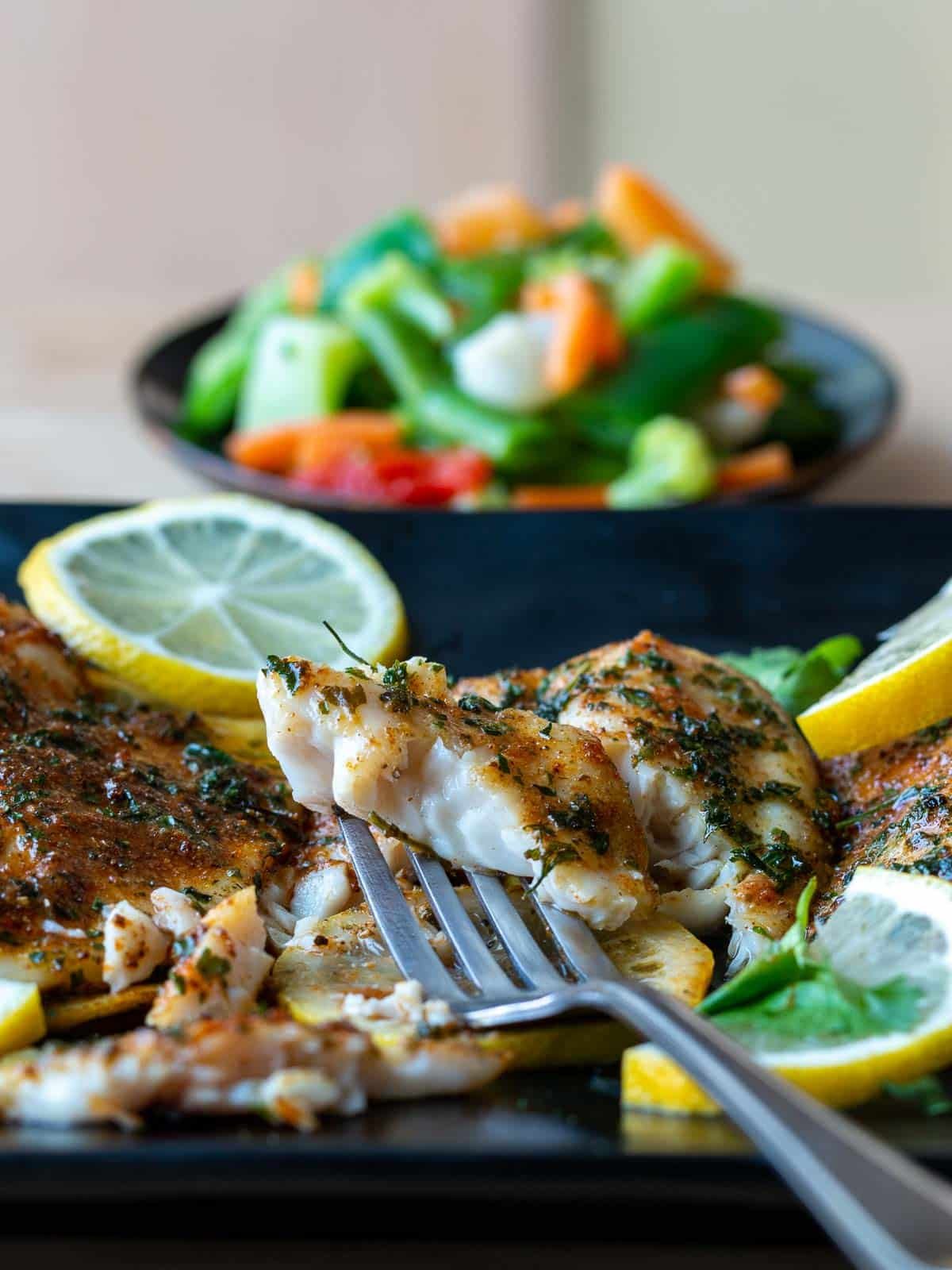 A bite of crispy but tender and flaky tilapia on a fork. 