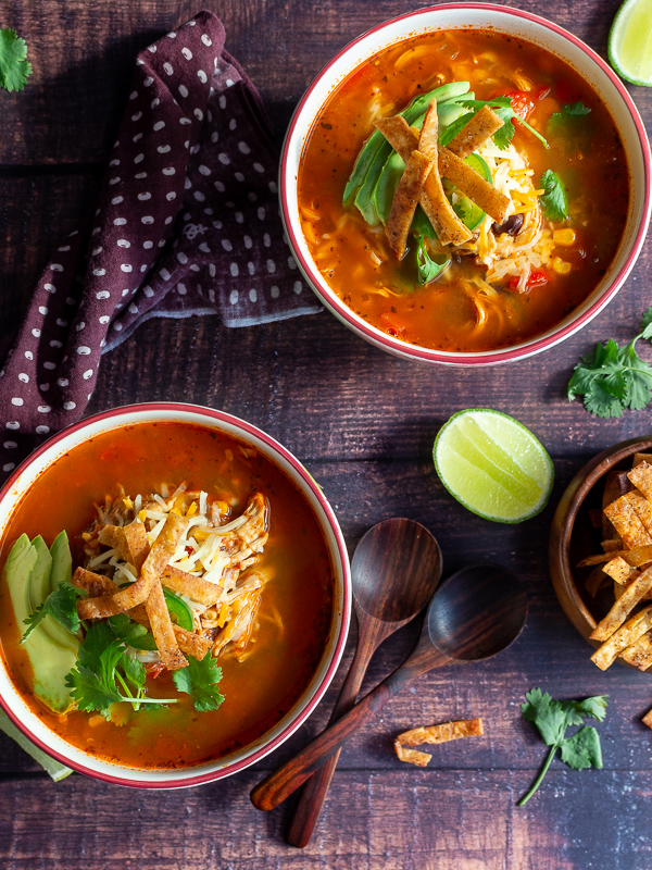 Two bowls of chicken tortilla soup with a lime and bowl of crispy tortilla strips