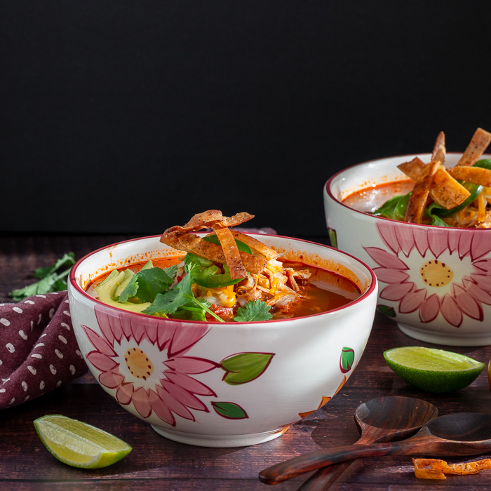 2 bowls of chicken tortilla soup with limes and garnishes.
