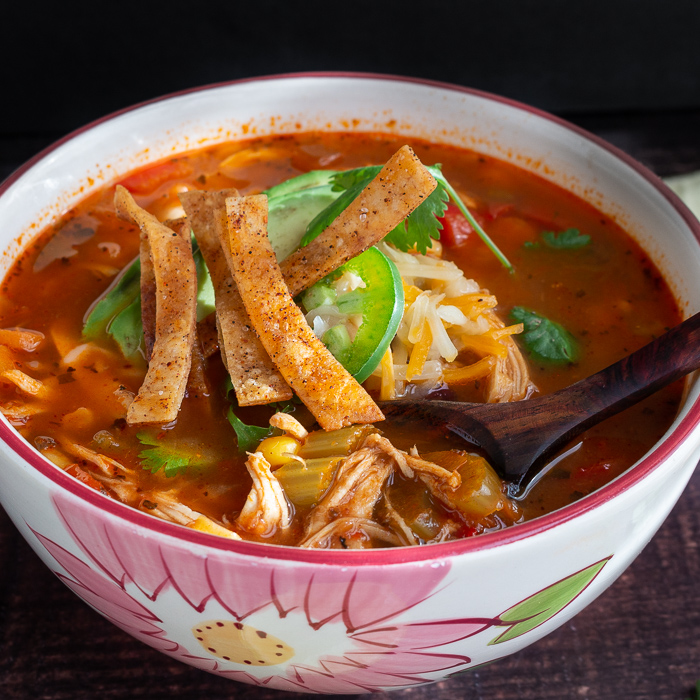 Bowl of Chicken Tortilla soup topped with baked tortilla strip with a wooden spoon grabbing a bite.