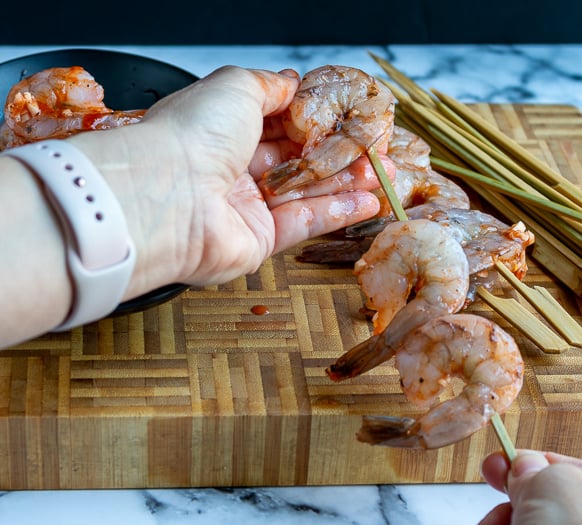 Marinated shrimp being placed on the skewer sticks.