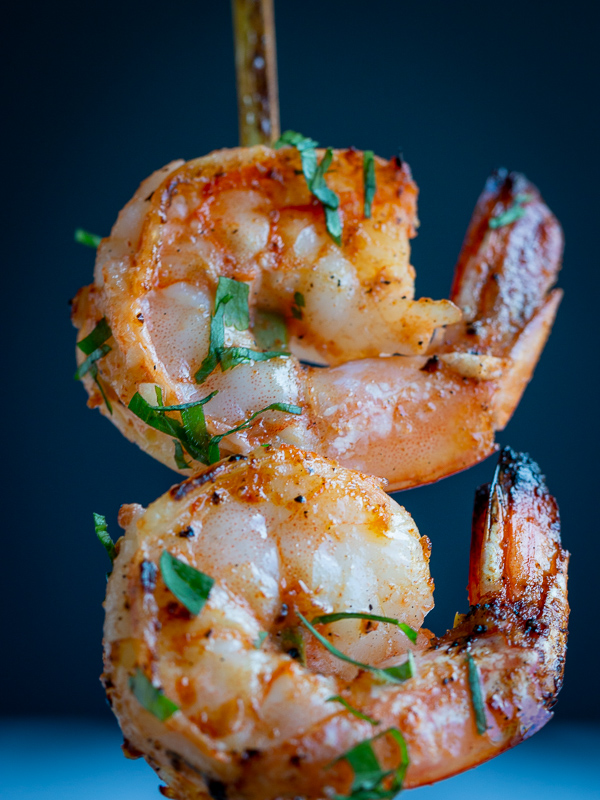 One shrimp skewer held in the air, cooked with 2 perfectly cooked shrimps with cilantro garnish. Super closeup.