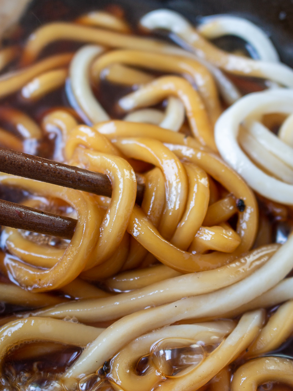 Udon noodles in a golden brown broth picked up with chopsticks.