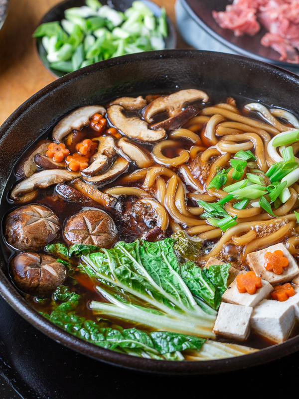 Sukiyaki Beef Udon with all the ingredients cooking in a black iron pot.