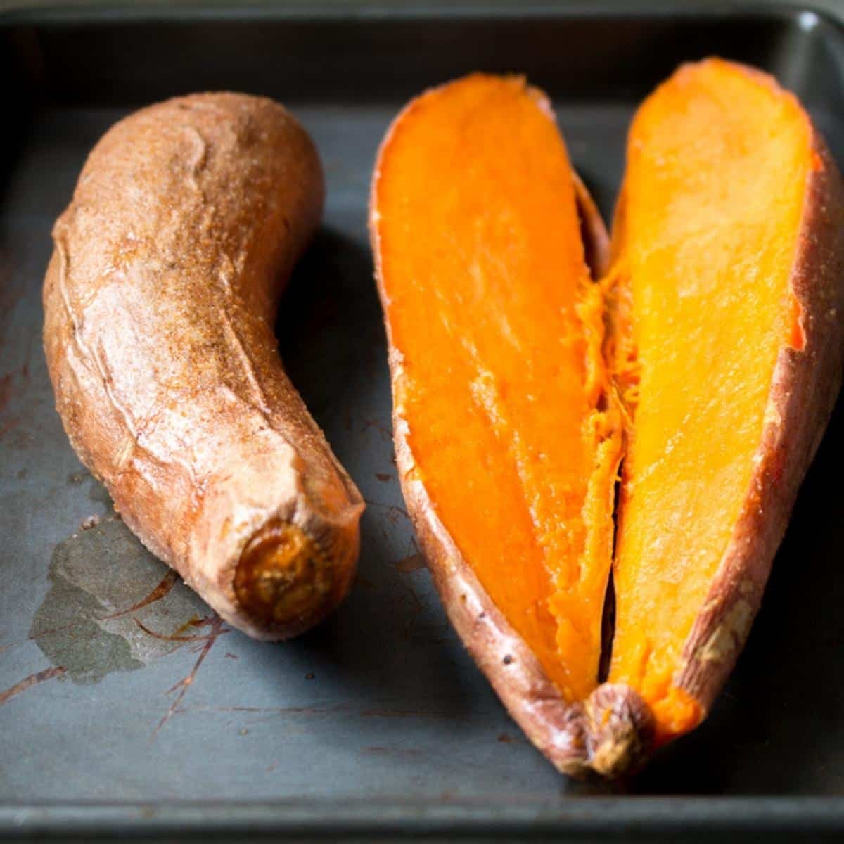 Roasted sweet potatoes on baking sheet with one sliced in half. 