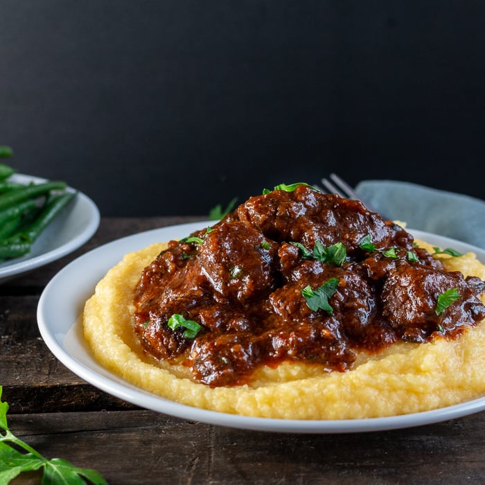 Tuscan Slow Cooked Braised Beef in Wine Sauce on a bed of polenta, garnished with parsley and a side of green beans. Super saucy and tender.