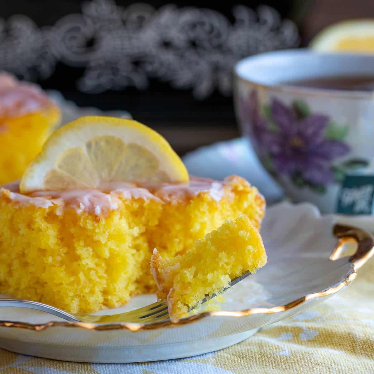 A bite out of a slice of lemon poke cake on a fork.